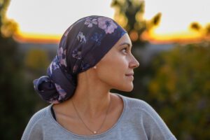 Eine starke Frau mit Kopftuch nach einer Chemotherapie-Behandlung schaut zuversichtlich in die Ferne, hinter ihr Pflanzen und der Sonnenuntergang