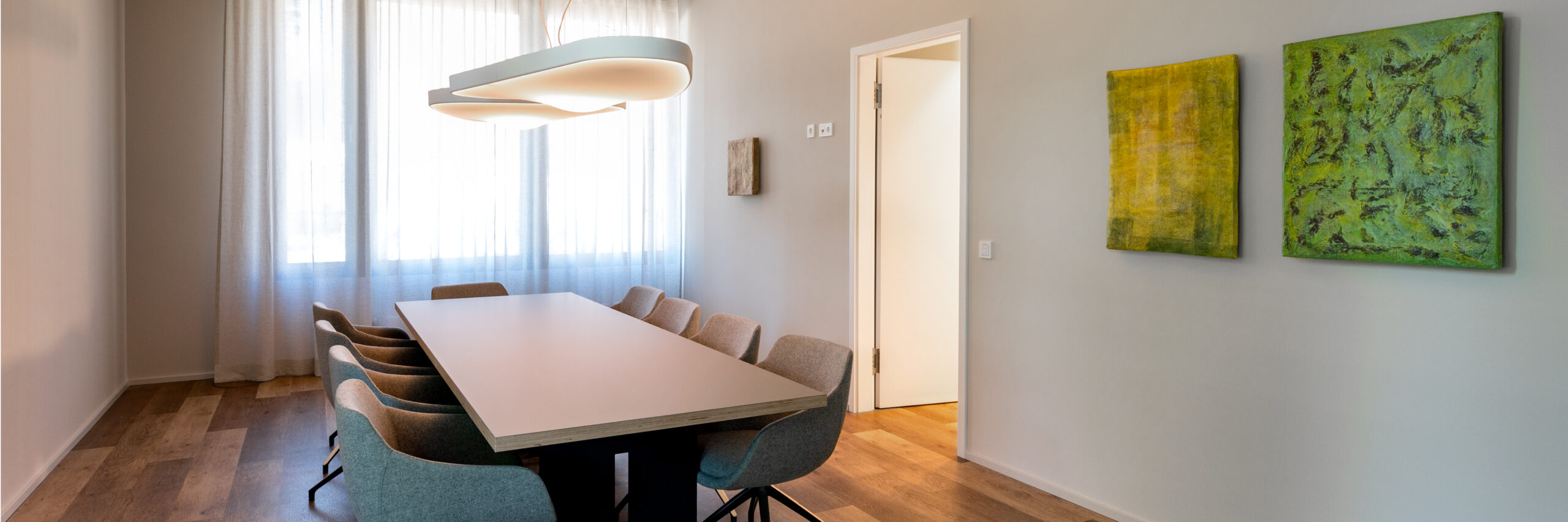 Heller Konferenzraum zur Besprechung der Brustkrebs-Früherkennung und Therapie der mamonova Praxis in Lindenthal mit großem Besprechungstisch, modernen Stühlen, natürlichem Tageslicht und stilvoller Wandgestaltung.